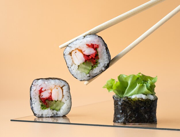 Фото Японские роллы на тарелке собирают палочками для еды на светло-оранжевом фоне