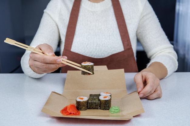 Japanese rolls with red fish in an open cardboard box on the table Girl eating sushi with chopsticks