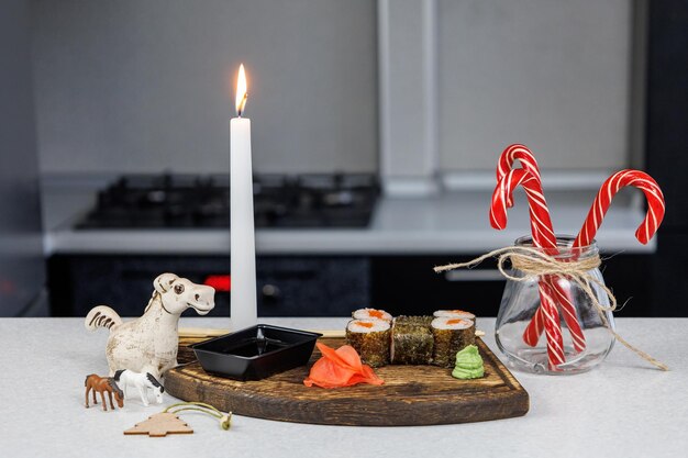 Japanese rolls with red fish on a wooden cutting board Table decoration with candles and sweets Christmas concept