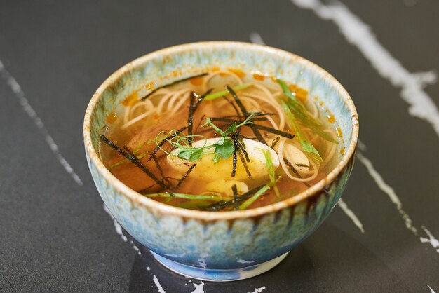 Japanese soup Ramen with egg and pork in a blue ceramic bowl on a black stone table