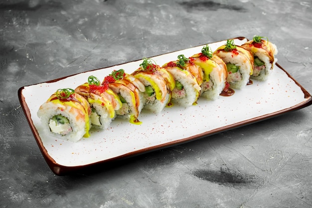 Japanese sushi roll with shrimp, cucumber, cream cheese and unagi sauce, tobiko caviar in a white plate on a gray table. Roll drenched in peach sauce