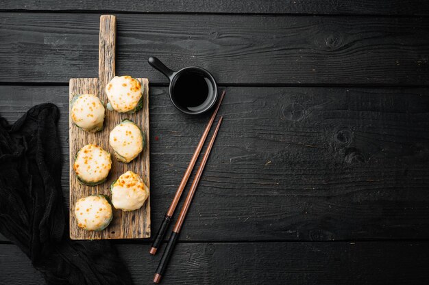 구운 에비(baked Ebi)라는 이름의 일본 스시 롤, 와사비와 연어 생선 세트, 검은 나무 테이블 배경, 위쪽 전망 플랫 레이, 카피스페이스 및 텍스트 공간