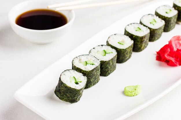 Japanese sushi rolls with cucumber, serving with soy sauce, wasabi and ginger on white background