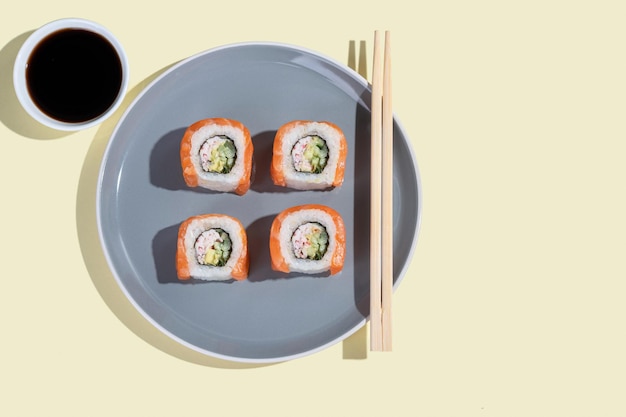 Japanese sushi with salmon dragon rolls on a bright yellow background Pop art Tasty snacks on a gray plate and chopsticks