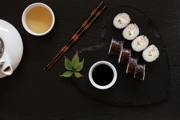 Japanese sushi with soy sauce on heart shape black  dish with chopsticks and traditional tea.