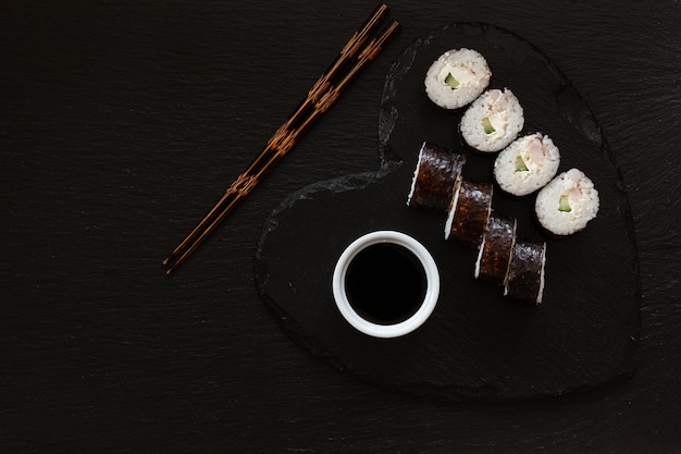 箸でハート形の黒い皿に醤油と日本の寿司。