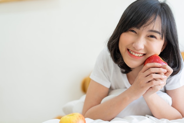 La ragazza giapponese dell'adolescente sorride con il benessere e tiene la mela rossa sul fronte per il concetto sano di stile di vita