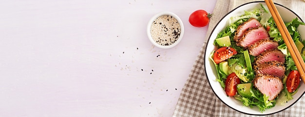 Insalata tradizionale giapponese con pezzi di tonno ahi alla griglia medio-raro e sesamo con verdure fresche su una ciotola.