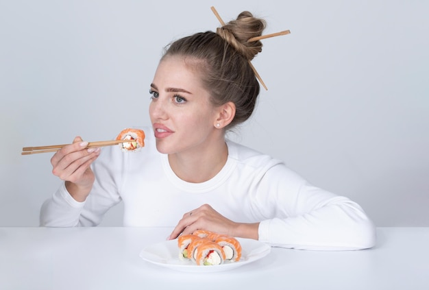 Японская женщина в стиле суши Ест японский набор суши Красота молодая женщина ест суши с палочками для еды, изолированными на белом Суши-ролл с палочками для еды Здоровая японская еда