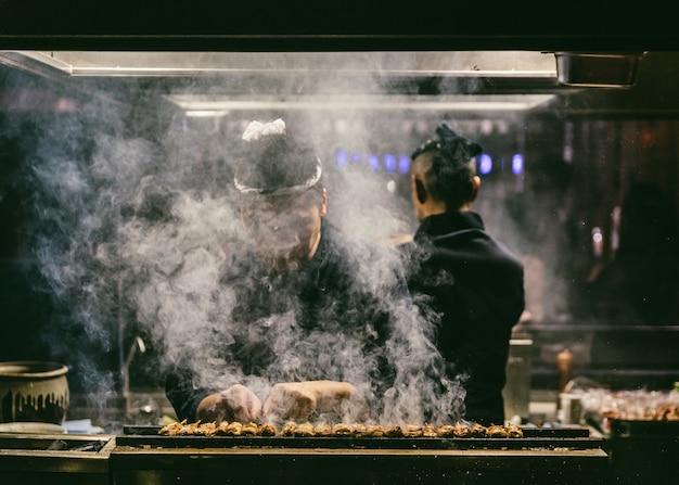 Japanese yakitori chef is grilling chicken with a lot of smoke.