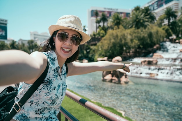 Japanese young woman travel in america. cheerful lady taking
selfie next to the pond and pointing finger to the water. girl
backpacker independent travel in las vegas.