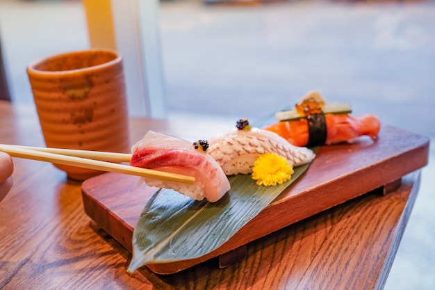 Japans eten, een set sushi op een rechthoekig houten bord, een stuk werd geplukt met stokjes en een kopje groene thee naast