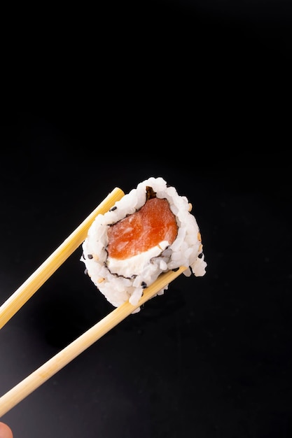 Japans eten met een zalmsushi met roomkaas met stokjes geïsoleerd op zwarte achtergrond