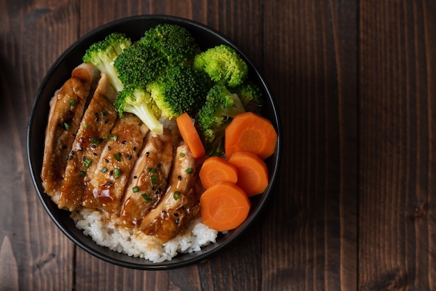 Japans eten stijl: bovenaanzicht van zelfgemaakte kip teriyaki gegrild met rijst, wortel, broccoli op de zwarte kom en plaats op houten tafel