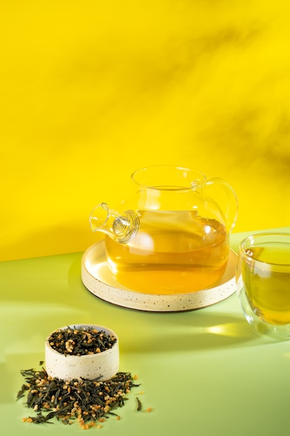 Japanse groene thee Genmaicha.Theebladeren met gebakken bruine rijst op een felgele achtergrond met een schaduw.Afslanktrend theeconcept. een kopje thee. brouw een transparante theepot