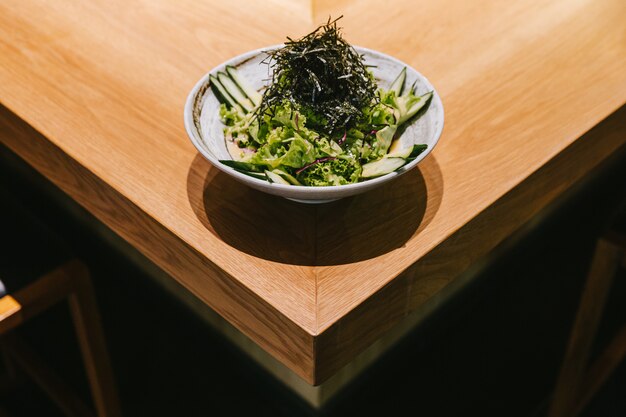 Japanse komkommersalade met sla, radijs en droog zeewier diende in ceramische kom op houten teller.