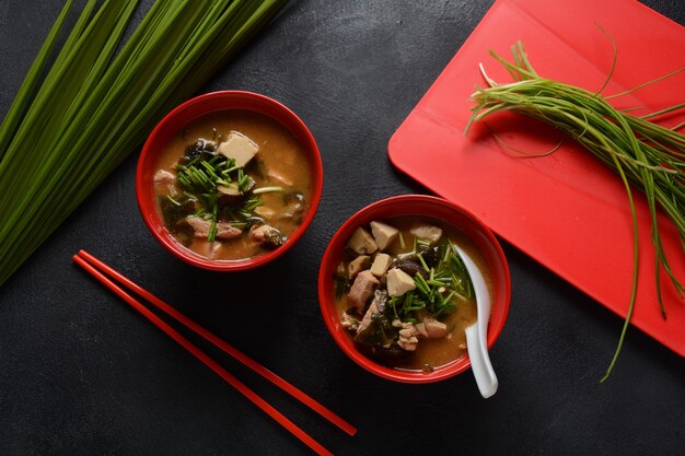 Japanse miso-soep in twee rode Japanse kommen op de zwarte tafel. Misosoep met tofu, tonijn, kruiden en zeewier met witte Japanse soeplepel en rode eetstokjes.