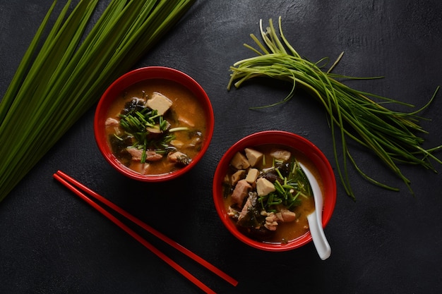 Japanse miso-soep in twee rode Japanse kommen op de zwarte tafel. Misosoep met tofu, tonijn, kruiden en zeewier met witte Japanse soeplepel en rode eetstokjes.