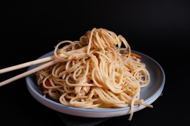 Japanse noedels met kip en sojasaus op een blauw bord op een zwarte achtergrond Schotel uit de Aziatische keuken