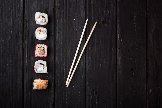 Japanse sushi rollen en eetstokjes liggend op een zwarte houten plank Uitzicht van bovenaf