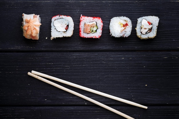 Japanse sushi rollen en eetstokjes liggend op een zwarte houten plank Uitzicht van bovenaf