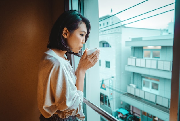 Japanse vrouw drinkt thee en kijkt door raam