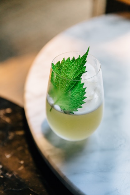 Japanse yuzu-cocktail met shiso-blaadjes (groene perilla) in glas op marmeren tafel.