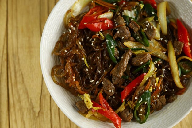 Japchae Korean Glass noodle stir fry Served in the bowl with wooden background
