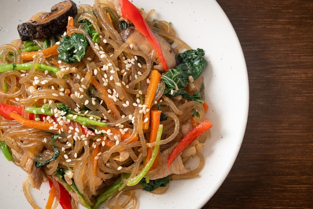 Japchae of geroerbakte Koreaanse vermicelli noedels met groenten en varkensvlees gegarneerd met witte sesam