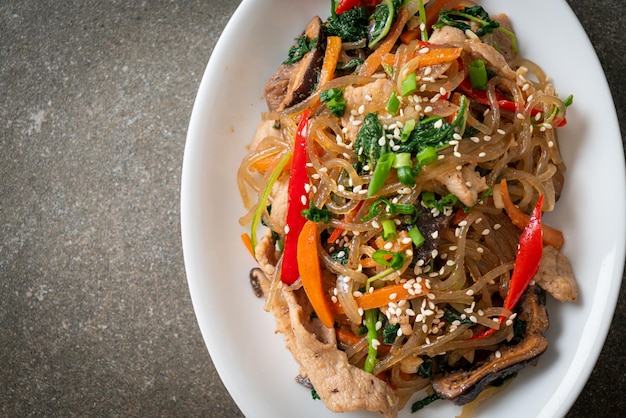 japchae or stir-fried Korean vermicelli noodles with vegetables and pork topped with white sesame - Korean traditional food style