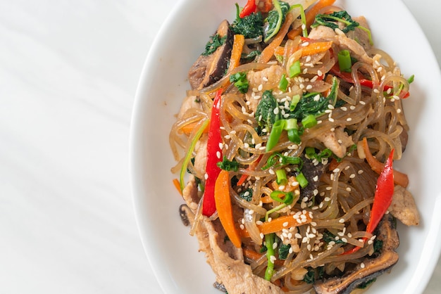 Japchae or stirfried Korean vermicelli noodles with vegetables and pork topped with white sesame