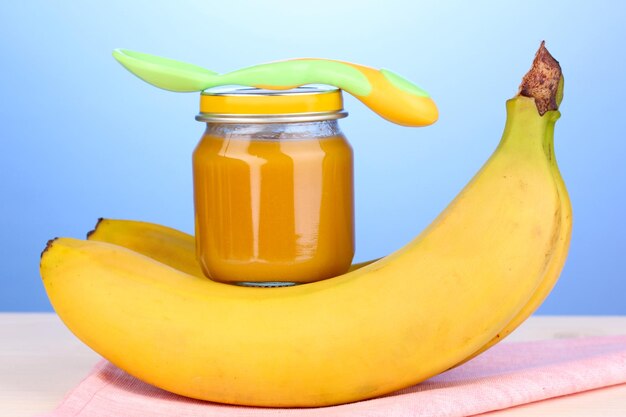 Jar of baby puree with spoon on napkin on blue background