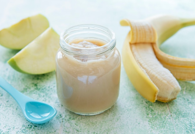 Jar of banana puree, apples and banana on green wooden table