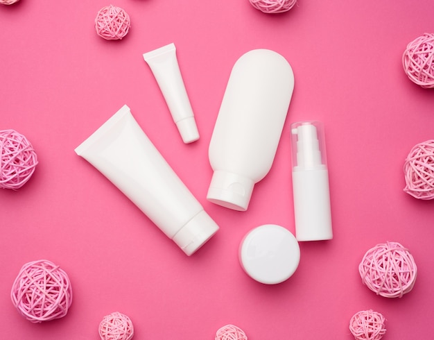 Jar, bottle and empty white plastic tubes for cosmetics on a pink background. Packaging for cream, gel, serum, advertising and product promotion, mock up