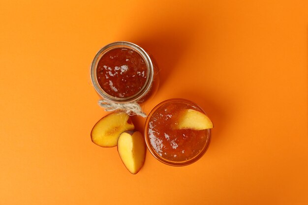 Jar and bowl of peach jam and ingredients on orange background