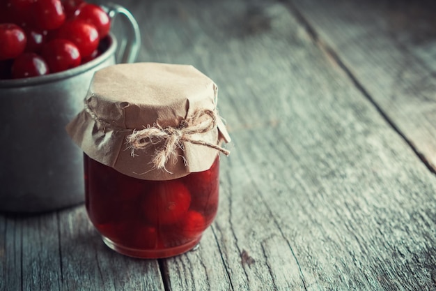 Jar of cherry jam and mug of ripe cherries not in focus on wooden table Copy space for text