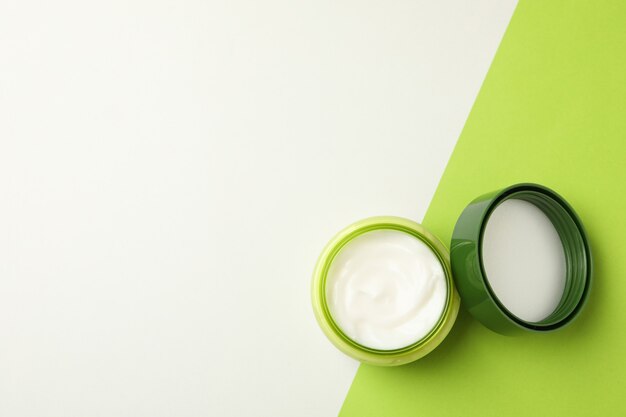 Jar of cosmetic cream and leaves on two tone background