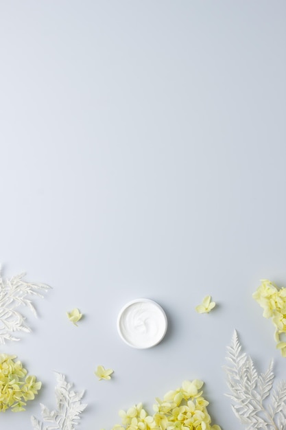 Jar of cosmetic cream with flowers on grey background Flat lay copy space