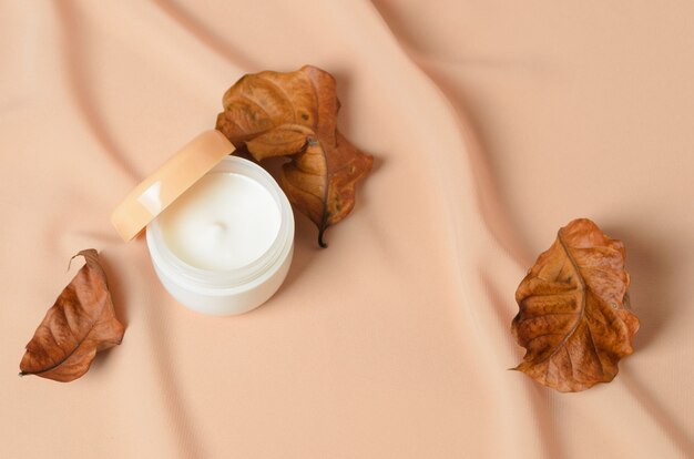 A jar of cream for dry skin care with dried autumn leaves. Selective focus.