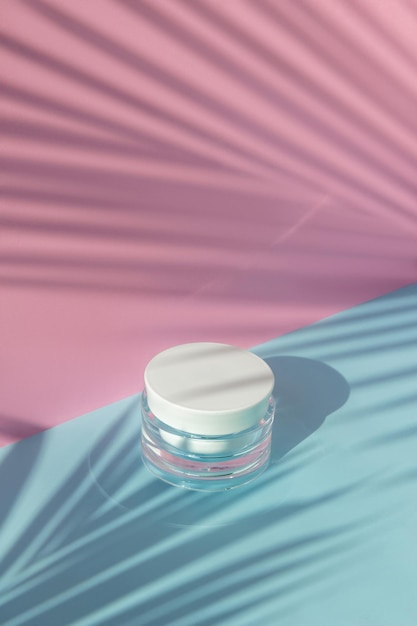 Jar of cream with palm leaf shadow on pink and blue background