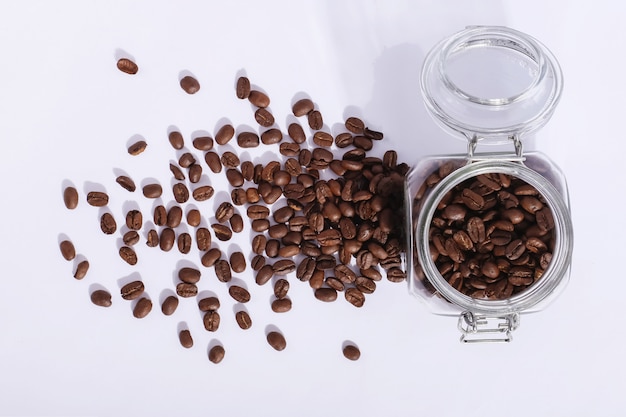 A jar of fresh fragrant coffee beans on white. Hard shadow from the sun, art concept of morning and energy charge