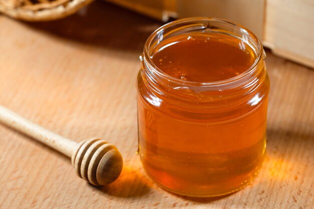 A jar of fresh honey and a honey ladle on a wooden table