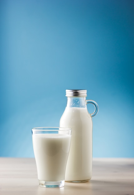 Jar and glass of milk on a wooden table and blue background