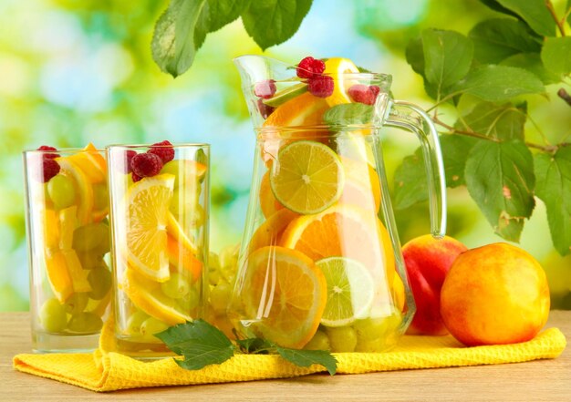 Jar and glasses with citrus fruits and raspberries on green background