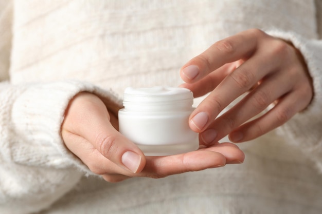 A jar of hand cream in hands on a light background