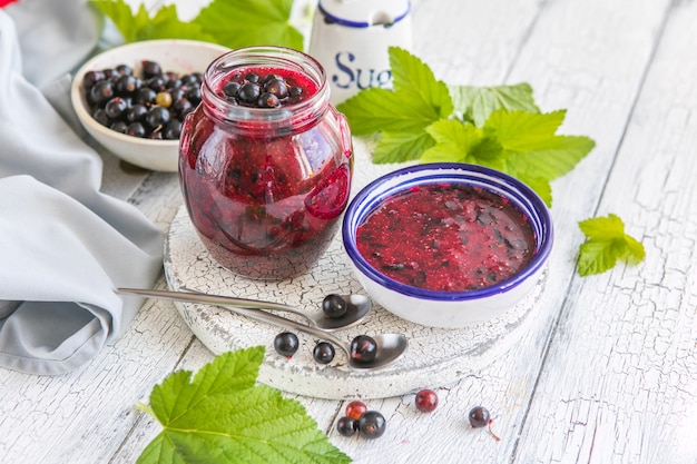 Jar of homemade fresh currant jam with shugar Fresh berries black currant on white wooden background