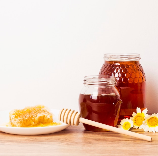 Jar of honey and honeycomb with honey dipper on wooden table