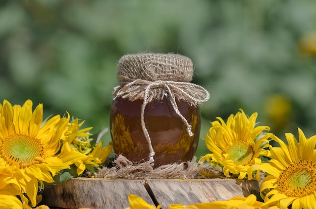 Jar of honey and sunflowers on wooden table over bokeh garden background Jar of fresh honey in field of wildflowers