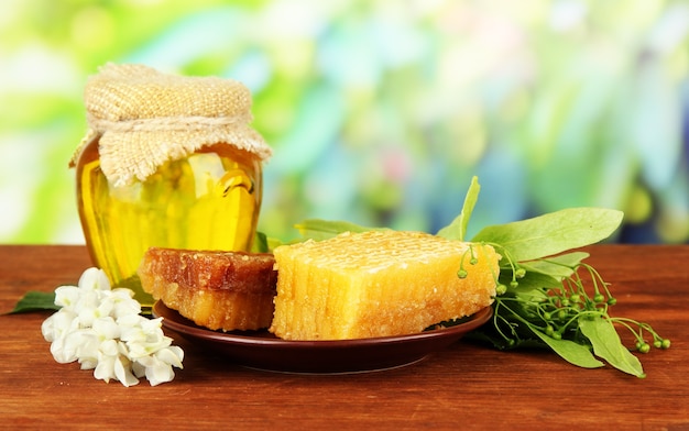 Jar of honey with flowers of lime, acacia on wooden table on defocused nature