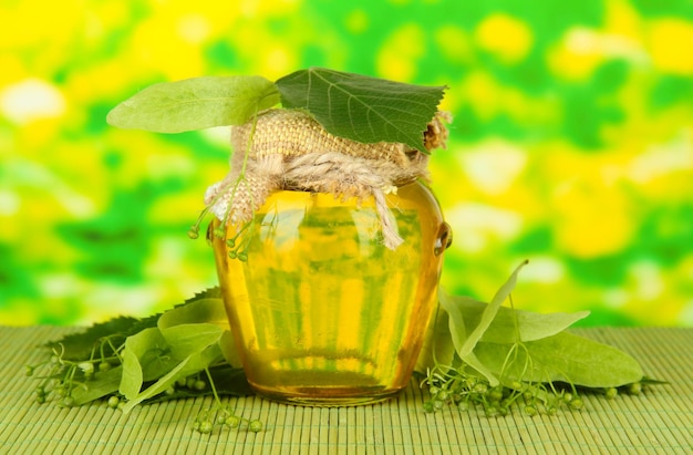 Jar of honey with flowers of lime on color bamboo mat on bright background